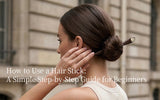 A minimal editorial image of a woman twisting her hair into a bun with a hair stick. Soft lighting and neutral tones highlight the simplicity and elegance of the styling process.